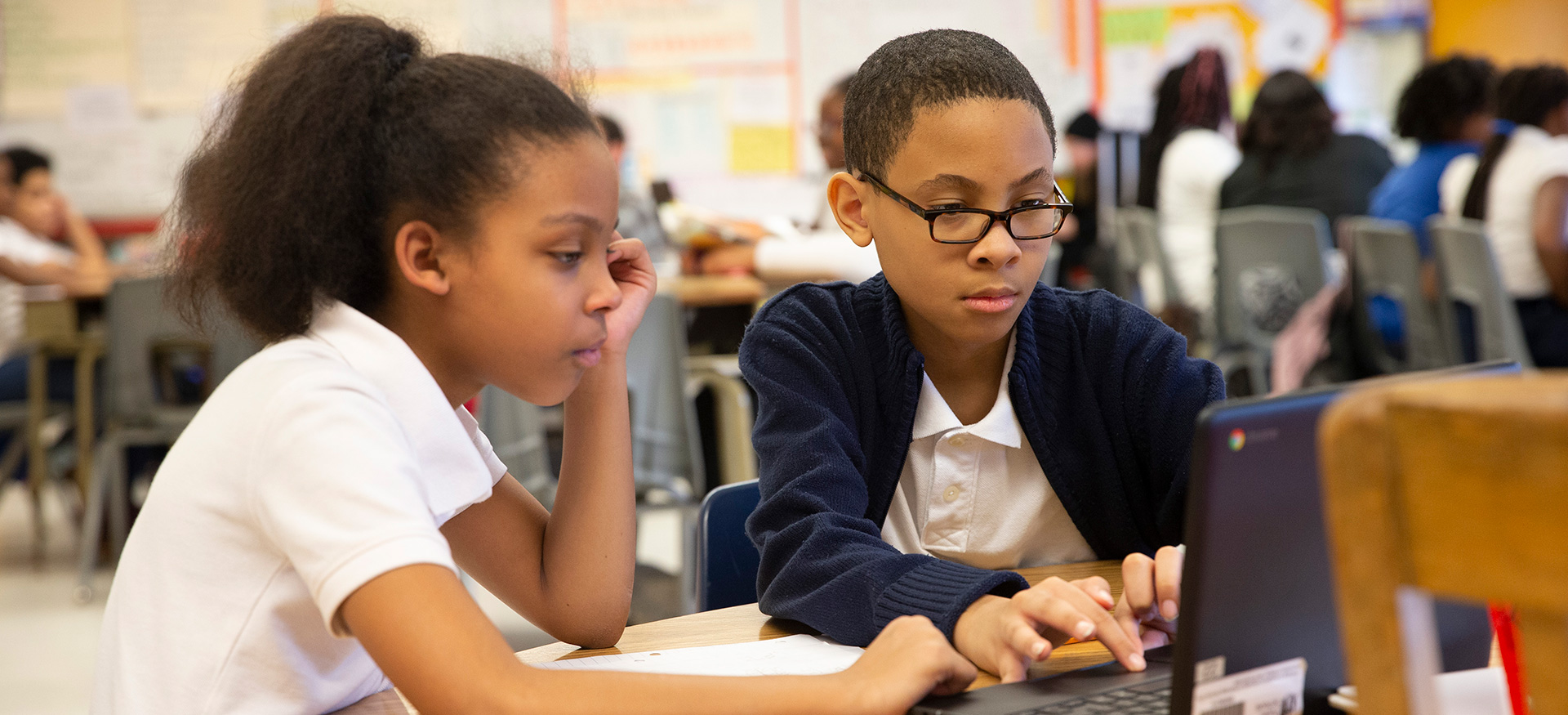 两个学生在教室里的一台笔记本电脑上一起工作。