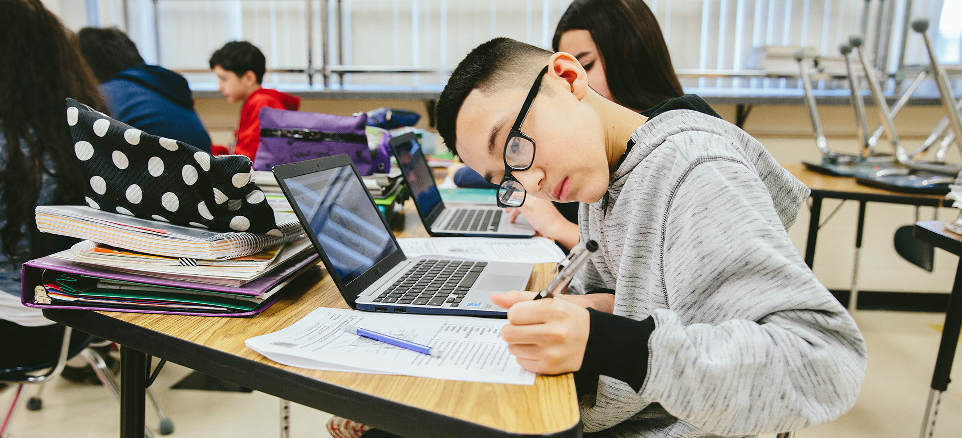 与笔记本电脑一起在书桌上独立工作的学生。一名学生在纸上写作。