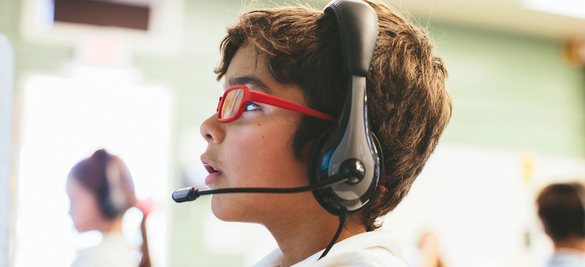 年轻的学生戴着耳机和眼镜抬头看电脑。